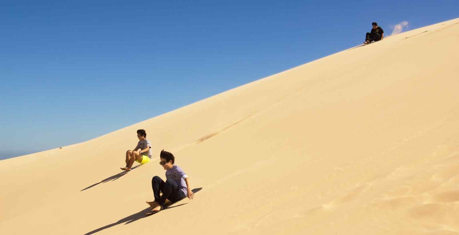 People sandboarding down sandunes