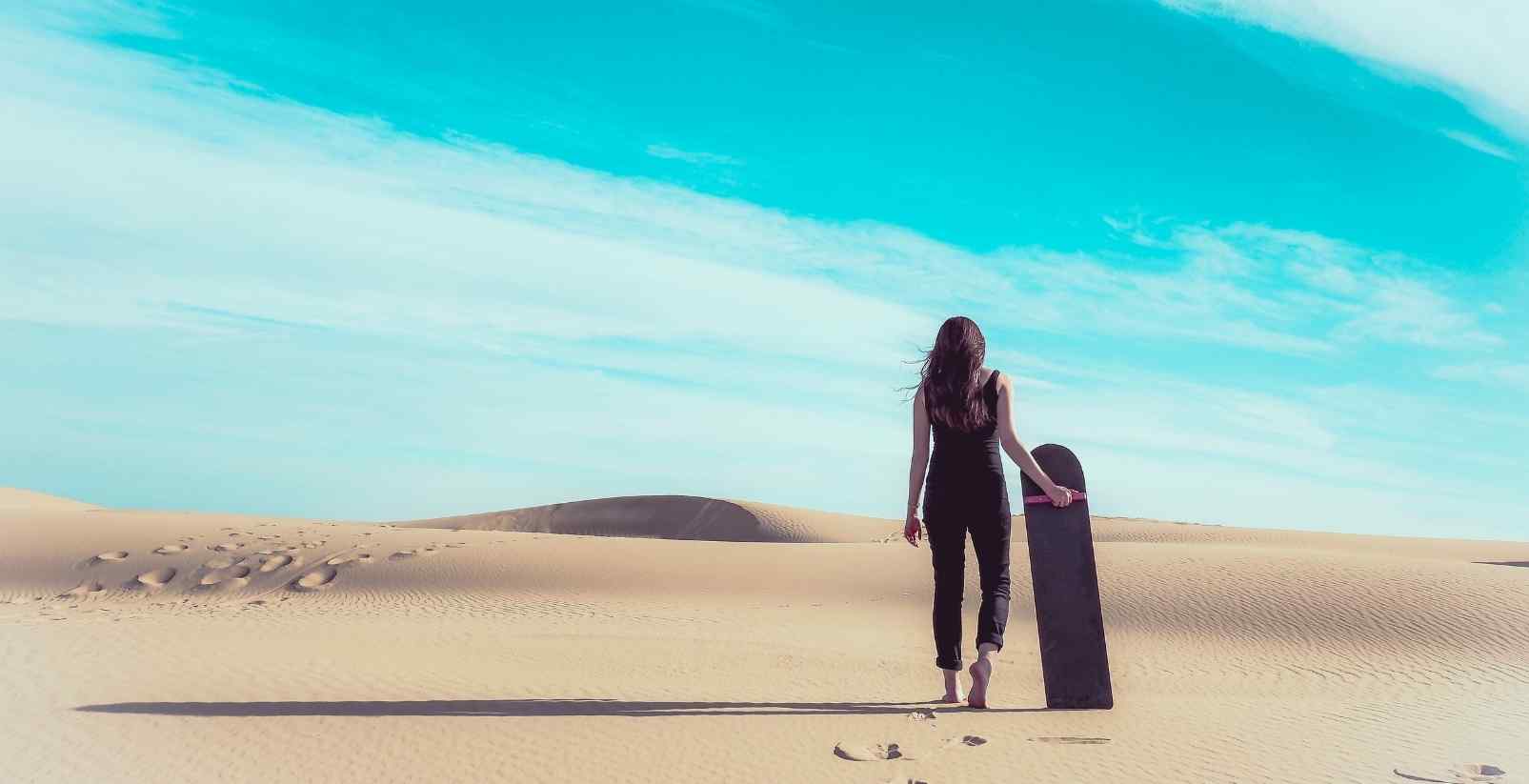 Woman holding sandboard in sand dunes
